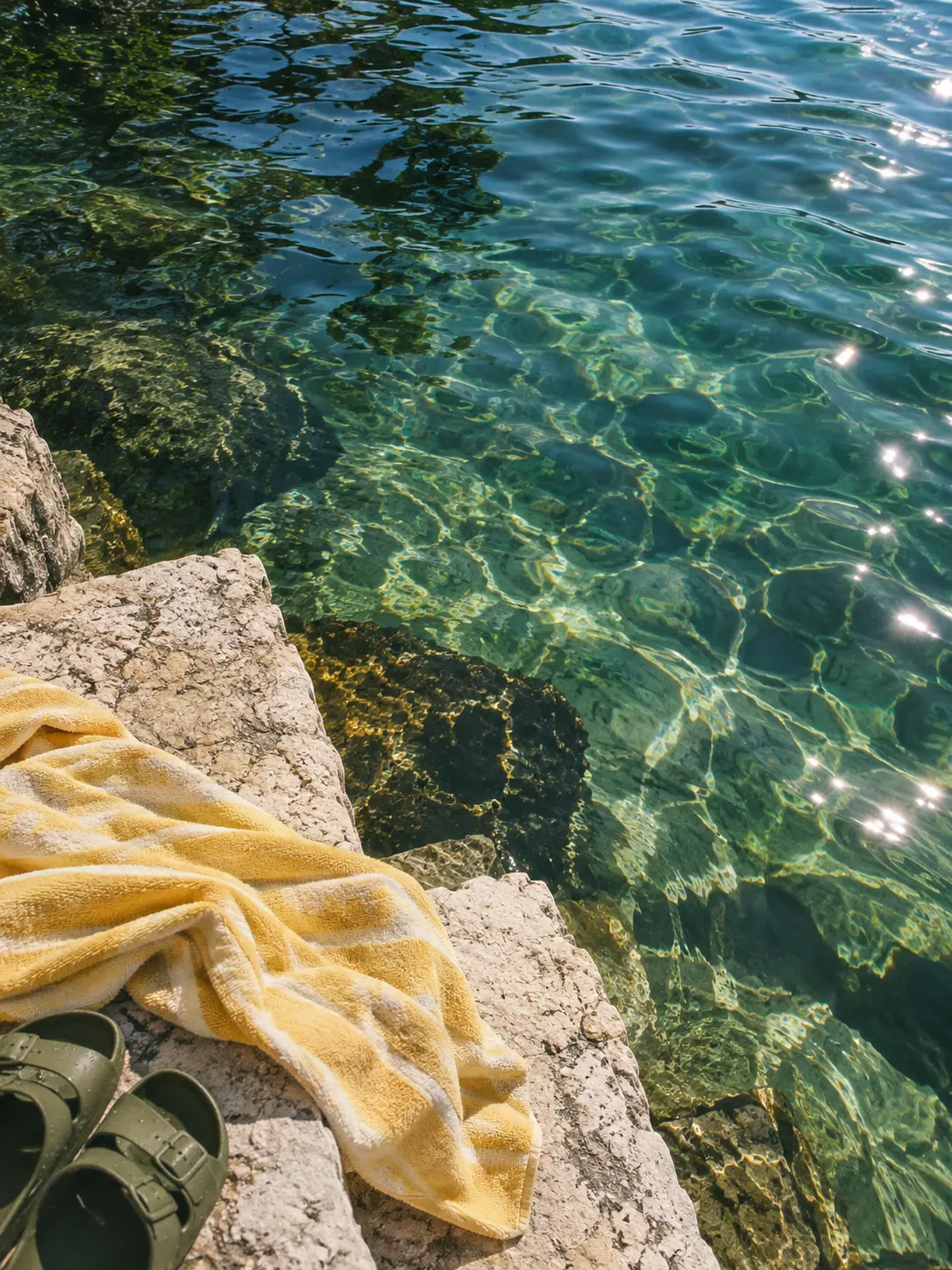 AI-created editorial image of clear lake water beside a stone step and yellow towel.